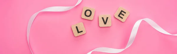 Top view of curved ribbon and wooden blocks with love lettering isolated on pink, panoramic shot — Stock Photo