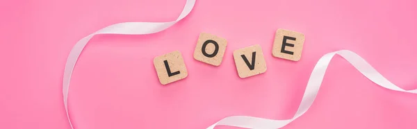 Top view of curved ribbon and wooden blocks with love lettering isolated on pink, panoramic shot — Stock Photo