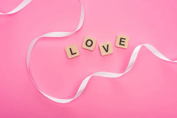 Top view of curved ribbon and wooden blocks with love lettering isolated on pink — Stock Photo