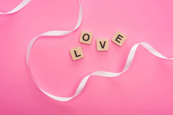 Top view of curved ribbon and wooden blocks with love lettering isolated on pink — Stock Photo