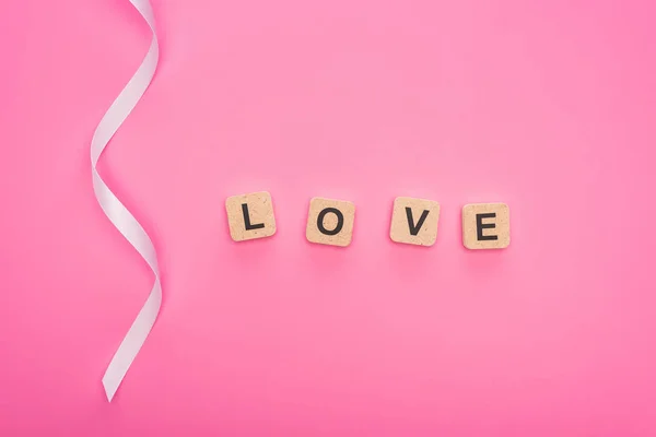 Vista superior de cinta curva y bloques de madera con letras de amor aisladas en rosa - foto de stock