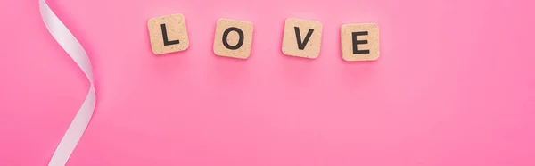 Top view of curved ribbon and wooden blocks with love lettering isolated on pink, panoramic shot — Stock Photo