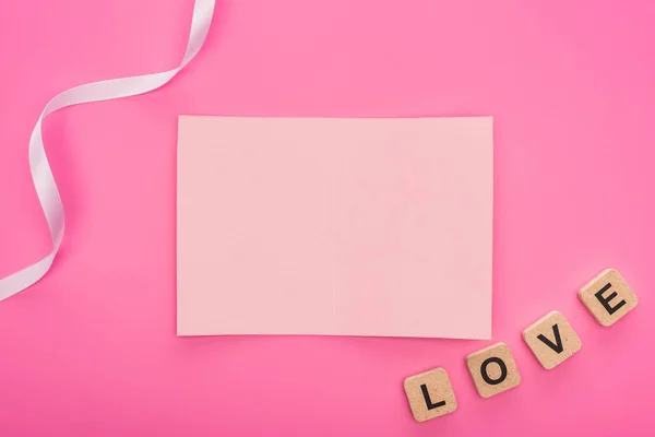Vue du dessus de la carte de papier vide avec ruban et lettrage d'amour sur cubes en bois isolés sur rose — Photo de stock