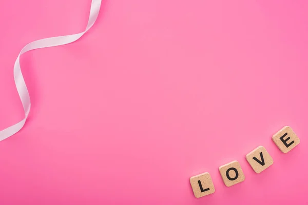 Top view of ribbon and love lettering on wooden cubes isolated on pink — Stock Photo