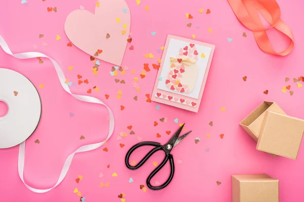 Top view of valentines confetti, empty compact disk, scissors, gift boxes, greeting card on pink background — Stock Photo