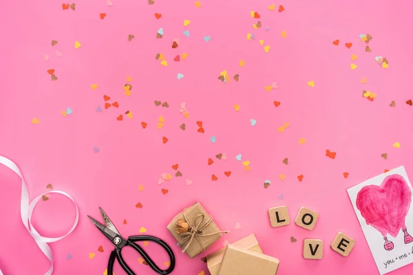 Top view of valentines confetti, empty compact disk, scissors, gift boxes, greeting card and cubes with love lettering on pink background — Stock Photo