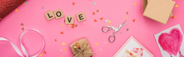 Top view of valentines confetti, scissors, wrapping paper, gift boxes, greeting cards and love lettering on wooden cubes on pink background, panoramic shot — Stock Photo