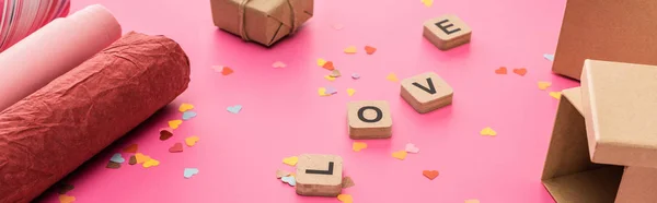 Valentine confetti, papel de embrulho, caixas de presente, letras de amor em cubos de madeira em fundo rosa, tiro panorâmico — Fotografia de Stock