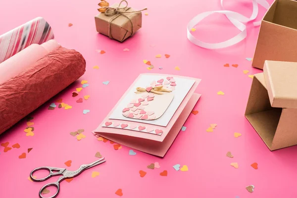 Valentine confetti, tesoura, cartão de felicitações, papel de embrulho, caixa de presente sobre fundo rosa — Fotografia de Stock