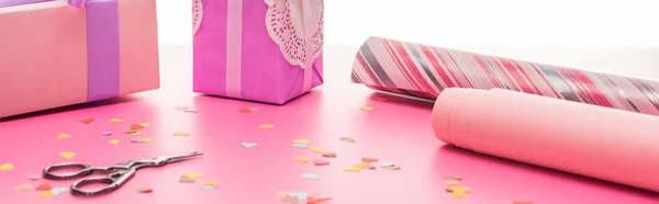 Valentines confetti, scissors, wrapping paper, gift boxes on pink surface isolated on white, panoramic shot — Stock Photo