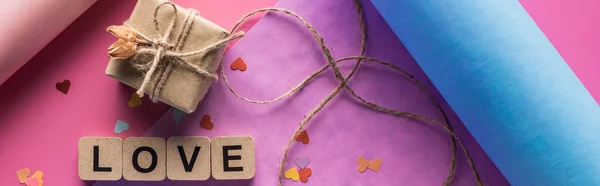 Vista superior de la decoración de San Valentín, papel de envolver, cordel, caja de regalo y letras de amor en cubos de madera sobre fondo rosa, plano panorámico — Stock Photo