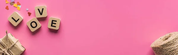 Верхний вид украшения валентинки, подарочная коробка, шпагат и любовь надписи на деревянных кубиках на розовом фоне, панорамный снимок — стоковое фото