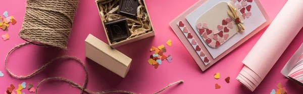 Vista dall'alto della decorazione di San Valentino, carta da regalo, spago, confezione regalo con cioccolato, biglietto di auguri su sfondo rosa, scatto panoramico — Foto stock