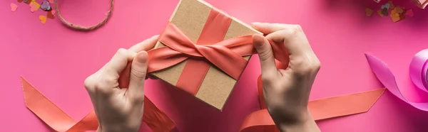 Partial view of woman decorating gift box with ribbon on pink background, panoramic shot — Stock Photo