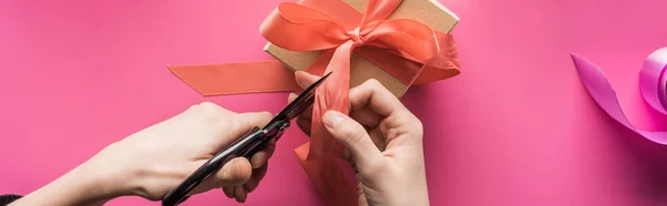 Vista recortada de la mujer cortando cinta mientras hace regalo de San Valentín sobre fondo rosa, tiro panorámico - foto de stock