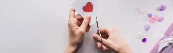 Vista ritagliata della donna ritaglio del cuore con le forbici vicino regalo di San Valentino su sfondo bianco, colpo panoramico — Foto stock