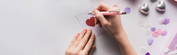 Vista recortada de la mujer escribiendo en tarjeta de San Valentín con el corazón sobre fondo blanco, plano panorámico - foto de stock