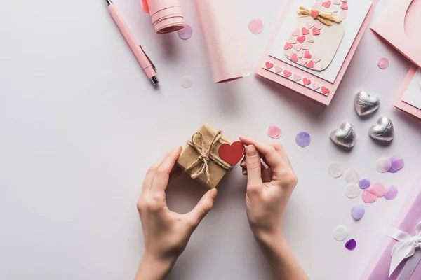 Vista recortada de la mujer que sostiene la caja de regalo de San Valentín con el corazón cerca de la decoración rosa sobre fondo blanco - foto de stock