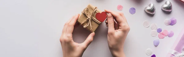 Vista recortada de la mujer que sostiene la caja de regalo de San Valentín con el corazón cerca de la decoración sobre fondo blanco, tiro panorámico - foto de stock