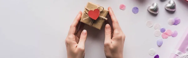 Vista recortada de la mujer que sostiene la caja de regalo de San Valentín con el corazón cerca de la decoración sobre fondo blanco, tiro panorámico - foto de stock