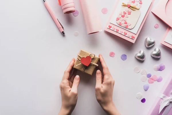 Vista recortada de la mujer que sostiene la caja de regalo de San Valentín con el corazón cerca de la decoración rosa sobre fondo blanco - foto de stock