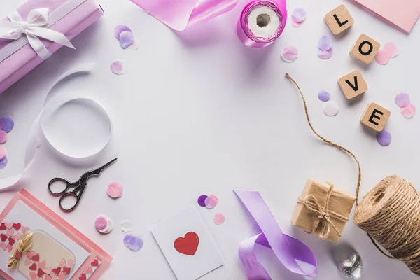 Vista superior de la decoración de San Valentín, regalos, suministros de mano y letras de amor en cubos sobre fondo blanco - foto de stock