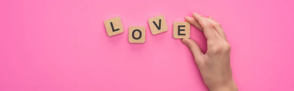Partial view of woman holding cubes with love lettering on pink background, panoramic shot — Stock Photo