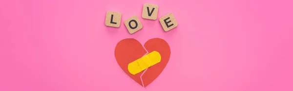 Top view of love lettering on wooden cubes near broken heart with patch on pink background — Stock Photo