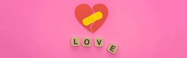 Top view of love lettering on wooden cubes near broken heart with patch on pink background — Stock Photo