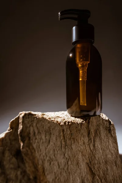Dispensador garrafa cosmética em pedra no fundo escuro com luz traseira — Fotografia de Stock