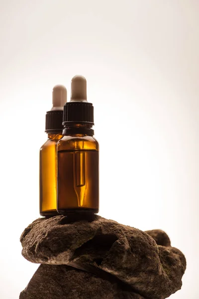 Cosmetic bottles with droppers on stone on white background with back light — Stock Photo