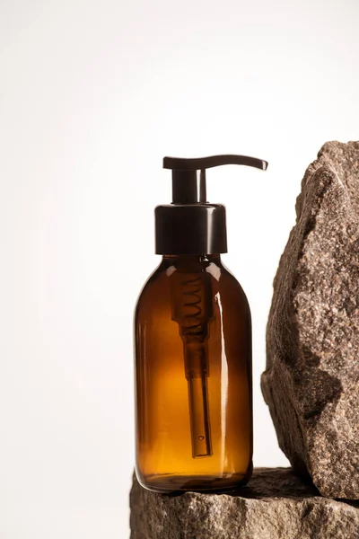 Dispenser cosmetic bottle on stones on white background with back light — Stock Photo