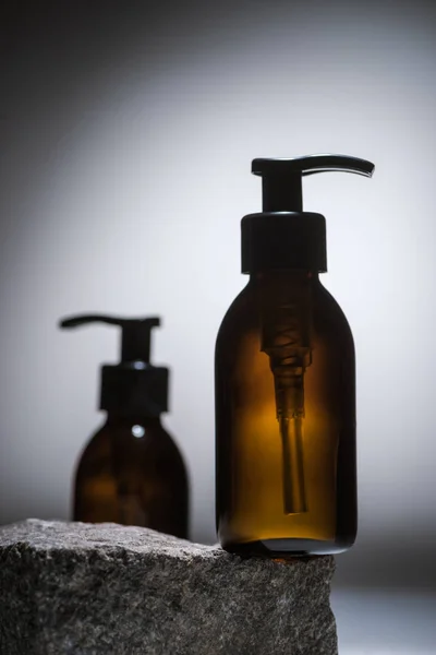 Selective focus of dispenser cosmetic bottles on stone on dark background with back light — Stock Photo