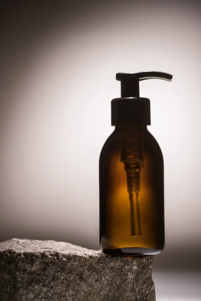 Distributeur bouteille cosmétique sur pierre sur fond sombre avec contre-jour — Photo de stock