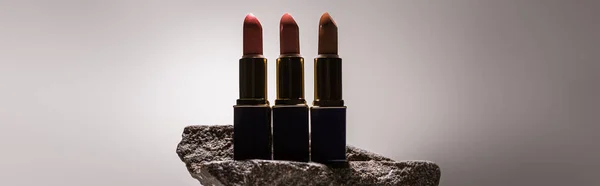 Lipsticks on stone in dark on white background with back light, panoramic shot — Stock Photo