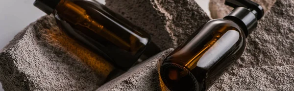 Dispenser cosmetic bottles on rocks isolated on grey, panoramic shot — Stock Photo