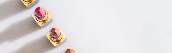 Draufsicht auf verschiedene Lippenstifte in Luxusröhren in einer Reihe auf weißem Hintergrund, Panoramaaufnahme — Stockfoto
