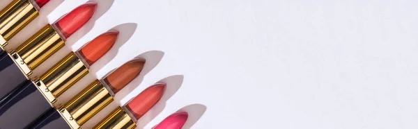 Vista dall'alto di rossetti assortiti in tubi di lusso in linea su sfondo bianco, scatto panoramico — Foto stock