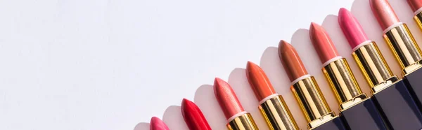 Top view of assorted lipsticks in luxury tubes in line on white background, panoramic shot — Stock Photo