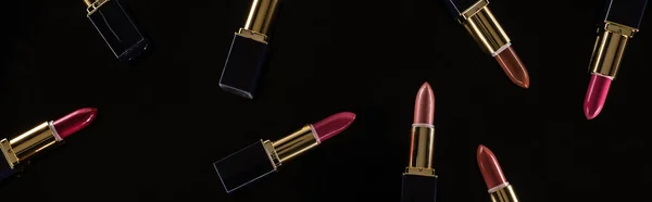 Top view of assorted lipsticks in luxury tubes isolated on black, panoramic shot — Stock Photo