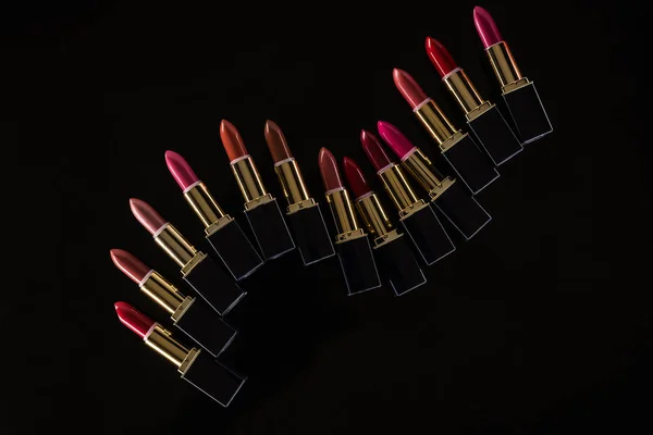 Vue de dessus des rouges à lèvres assortis dans des tubes de luxe isolés sur noir — Photo de stock
