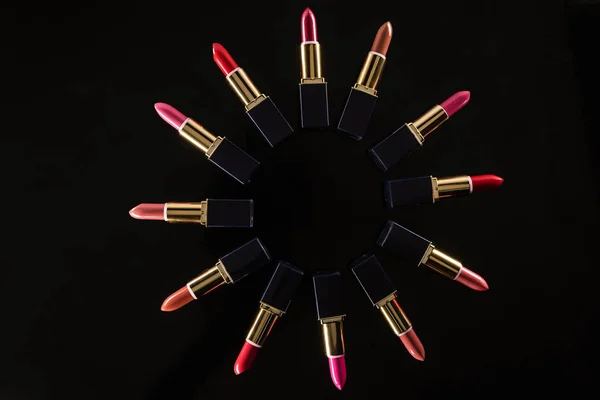 Top view of assorted lipsticks in luxury tubes arranged in circle isolated on black — Stock Photo