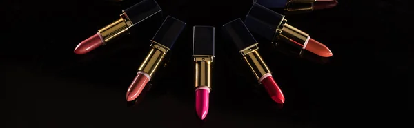 Verschiedene Lippenstifte in Luxusröhrchen, kreisförmig angeordnet, isoliert auf schwarzer, panoramischer Aufnahme — Stockfoto