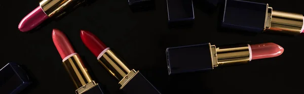 Top view of assorted lipsticks in luxury tubes scattered isolated on black, panoramic shot — Stock Photo