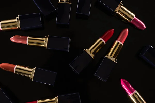 Top view of assorted lipsticks in luxury tubes scattered isolated on black — Stock Photo