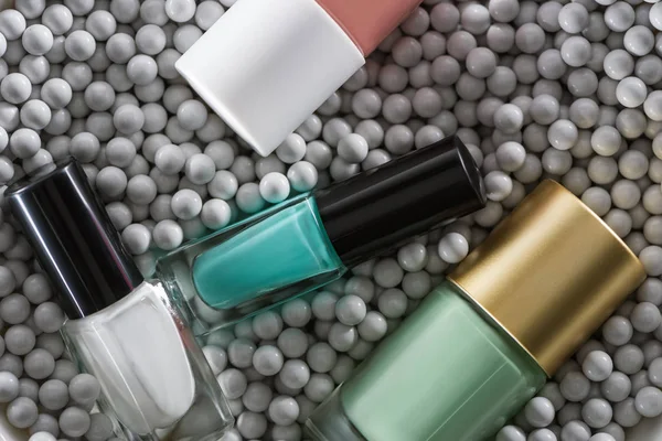 Top view of assorted nail polish in bottles in grey decorative beads — Stock Photo