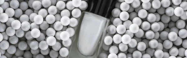 Top view of white nail polish in bottle among grey decorative beads, panoramic shot — Stock Photo