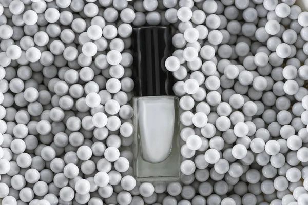 Верхний вид белого лака для ногтей в бутылке среди серых декоративных бусин — стоковое фото