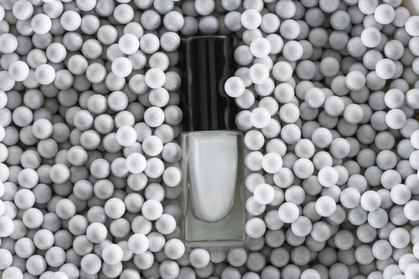 Top view of white nail polish in bottle among grey decorative beads — Stock Photo