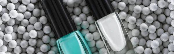 Top view of blue and white nail polish in bottles in grey decorative beads, panoramic shot — Stock Photo